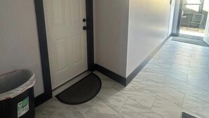 Un couloir avec une porte blanche, une poubelle et un paillasson.