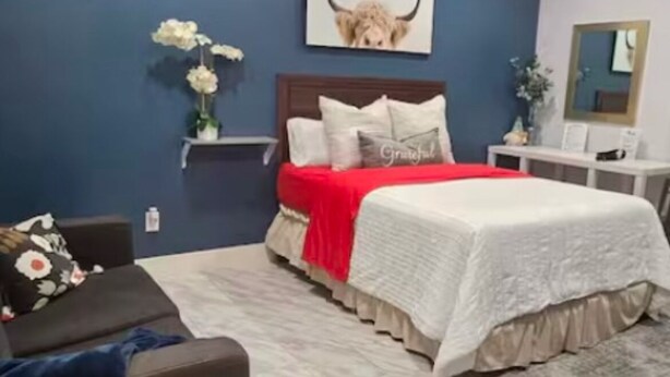 Une chambre à coucher comprenant un lit, une table de chevet, une chaise et une étagère fixée au mur.