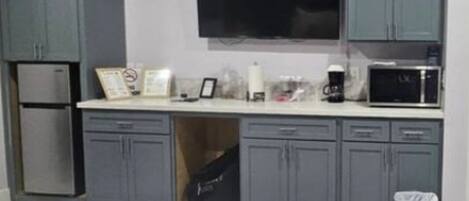 Une chambre compacte comprenant un lit, une kitchenette équipée d’un réfrigérateur et d’un micro-ondes, ainsi qu’un téléviseur fixé au mur.