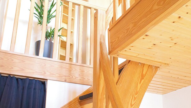 Una escalera de madera con barandilla que lleva a un nivel superior con una planta en maceta.