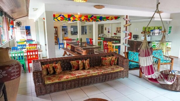 A cozy living area with a wicker sofa, colorful chairs, and a hanging hammock. - Pousada Flor de Porto (Ipojuca)