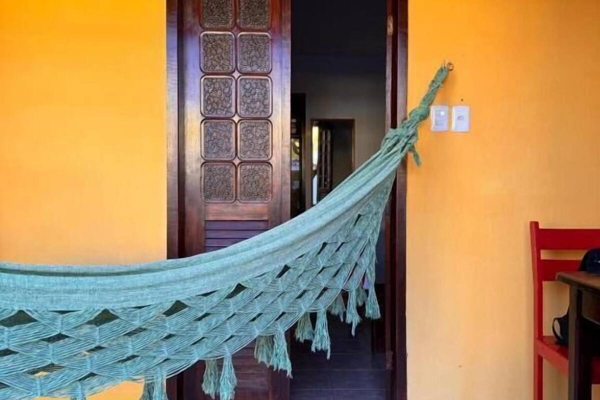 Un hamac est attaché au cadre d’une porte dans une pièce dont le sol est carrelé et un des murs est jaune.