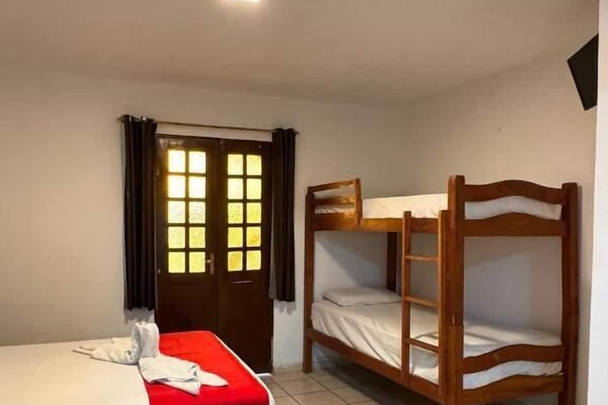 Une chambre avec un lit simple, un lit superposé, une porte avec une fenêtre et un sol carrelé.