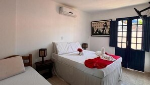 A hotel room with two beds, a ceiling fan, an air conditioning unit, a window with curtains, and a painting on the wall. - Pousada Flor de Porto (Ipojuca)
