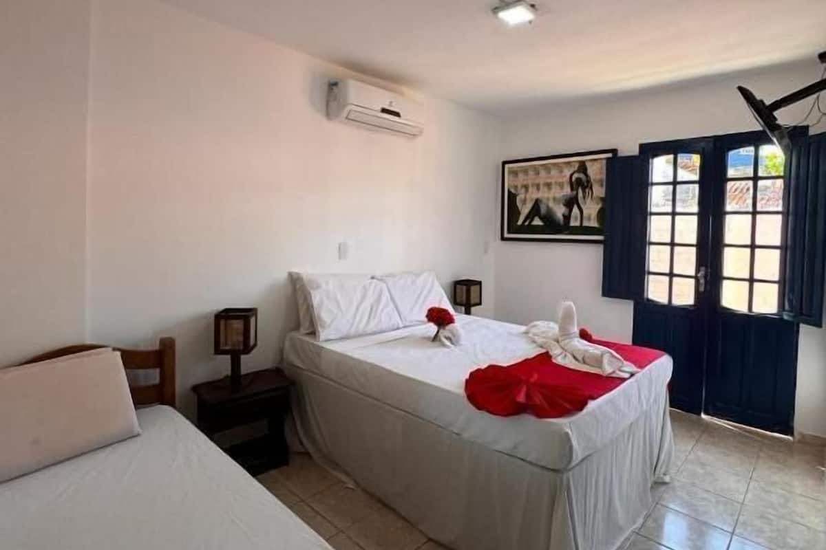 Une chambre d’hôtel avec deux lits, un ventilateur de plafond, un appareil de climatisation, une fenêtre avec des rideaux et un tableau au mur.