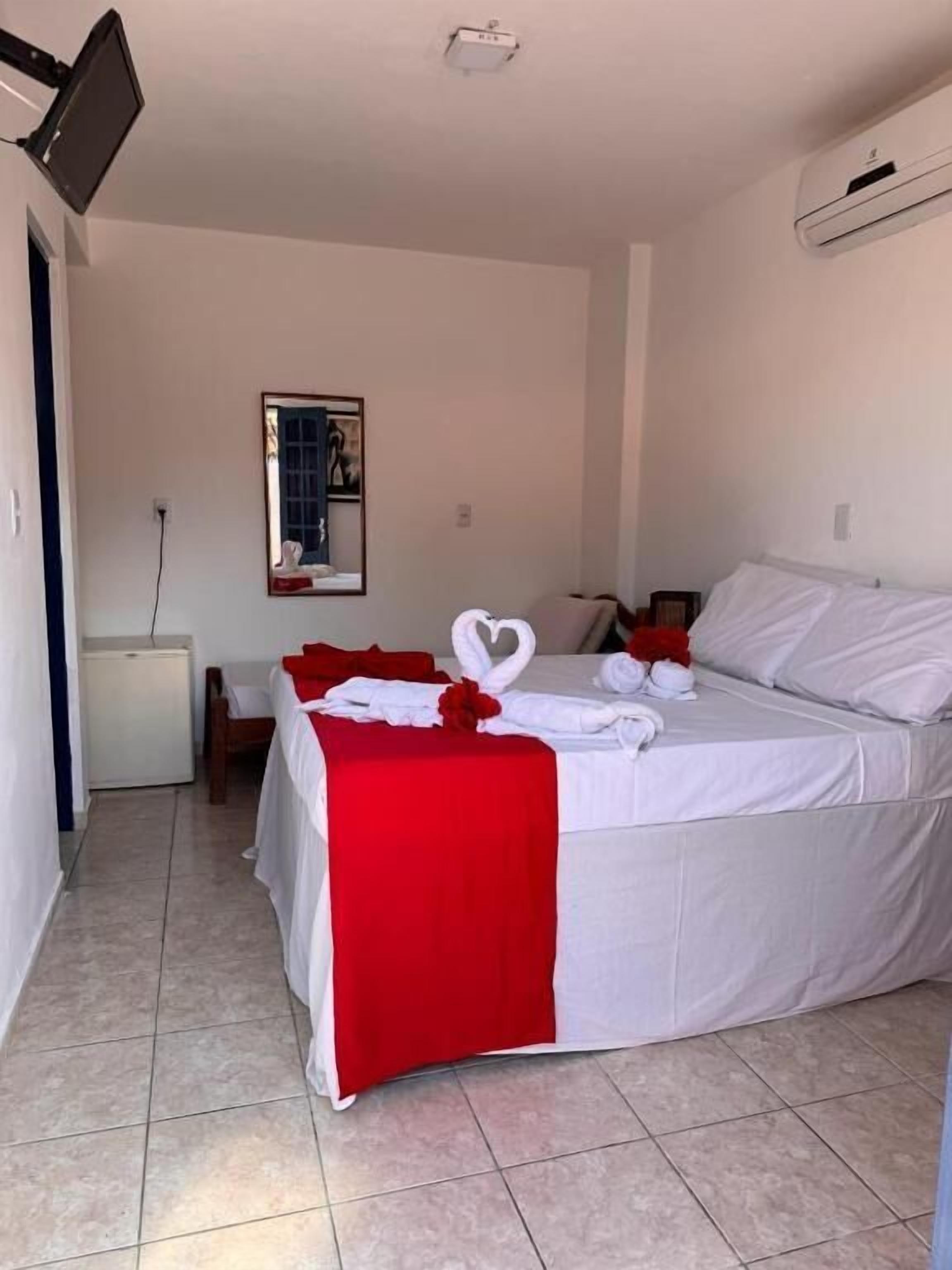 A hotel room with a bed, a desk, a chair, a small table, a wall-mounted TV, and a framed picture on the wall.