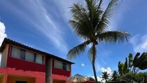 A swimming pool with lounge chairs, a palm tree, and a red building with a tiled roof. - Pousada Flor de Porto (Ipojuca)