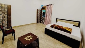 Un dormitorio con una cama, una silla, una mesita pequeña, un ventilador de techo y una puerta con cortinas estampadas.