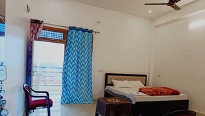 Un dormitorio con cama, una silla, una mesita y un ventanal con cortinas.