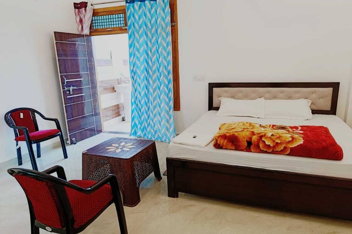 Un dormitorio con cama, una silla, una mesita y una ventana con cortinas.