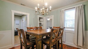 Comedor con mesa y sillas de madera, un candelabro y una ventana con cortinas.