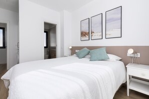 A modern bedroom with a large bed, white walls, and three framed pictures on the wall.