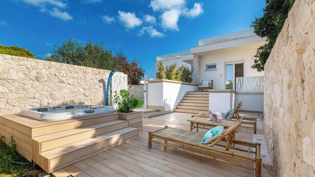 Une terrasse en bois avec un jacuzzi, des chaises longues et un mur en pierre.