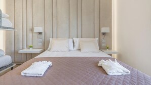Une chambre d’hôtel avec un grand lit, deux tables de chevet, une tête de lit et deux lampes fixées au mur.