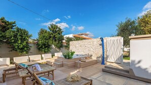 Une terrasse extérieure ensoleillée, dotée de chaises longues en bois, d’un mur en pierre et d’un jacuzzi.