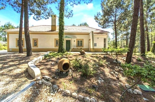 A two-story house with a tiled roof, surrounded by trees and a landscaped garden.