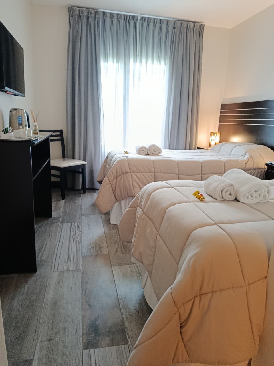 Quarto de hotel com duas camas, uma escrivaninha e uma cadeira.