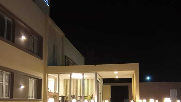 Una entrada de hotel moderna con un camino bien iluminado, ventanas amplias y un letrero visible que dice 'Hotel'.