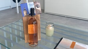 Une bouteille de vin, une bougie et une carte de bienvenue sur une table en verre dans une cuisine moderne.