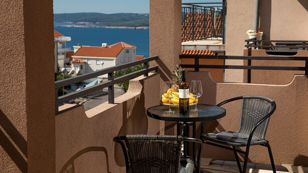 A balcony with a table set for two, featuring a bottle of wine, two glasses, and a fruit bowl with bananas and a pineapple. - Charming studio with sea view, bikes, baby crib, barbecue (Crikvenica)
