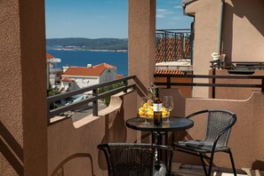 A balcony with a table set for two, featuring a bottle of wine, two glasses, and a fruit bowl with bananas and a pineapple. - Charming studio with sea view, bikes, baby crib, barbecue (Crikvenica)