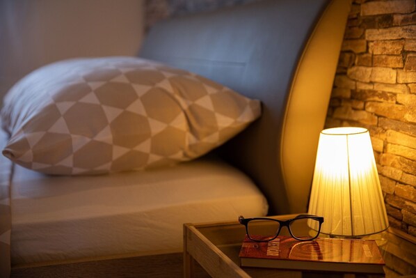 A neatly made bed with patterned pillows, a bedside lamp, and a book with glasses on a wooden nightstand. - Charming studio with sea view, bikes, baby crib, barbecue (Crikvenica)