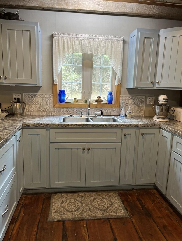 A kitchen with white cabinets, a double sink, and a window with a curtain.
