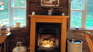 L’intérieur d’un chalet chaleureux, avec une cheminée, des murs en bois et deux fenêtres ornées de rideaux à carreaux.