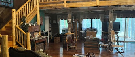 A spacious living room with a wooden staircase, a cozy fireplace, and a large window offering a view of the outdoors.