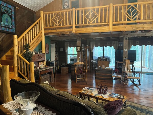 A spacious living room with a wooden staircase, a cozy fireplace, and a large window offering a view of the outdoors.
