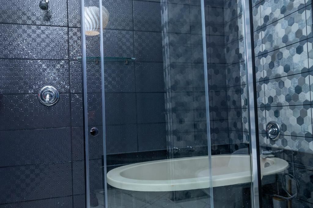 Ein Badezimmer mit einer gläsernen Duschkabine, einem weißen Waschbecken und dunkel gemusterten Fliesen.