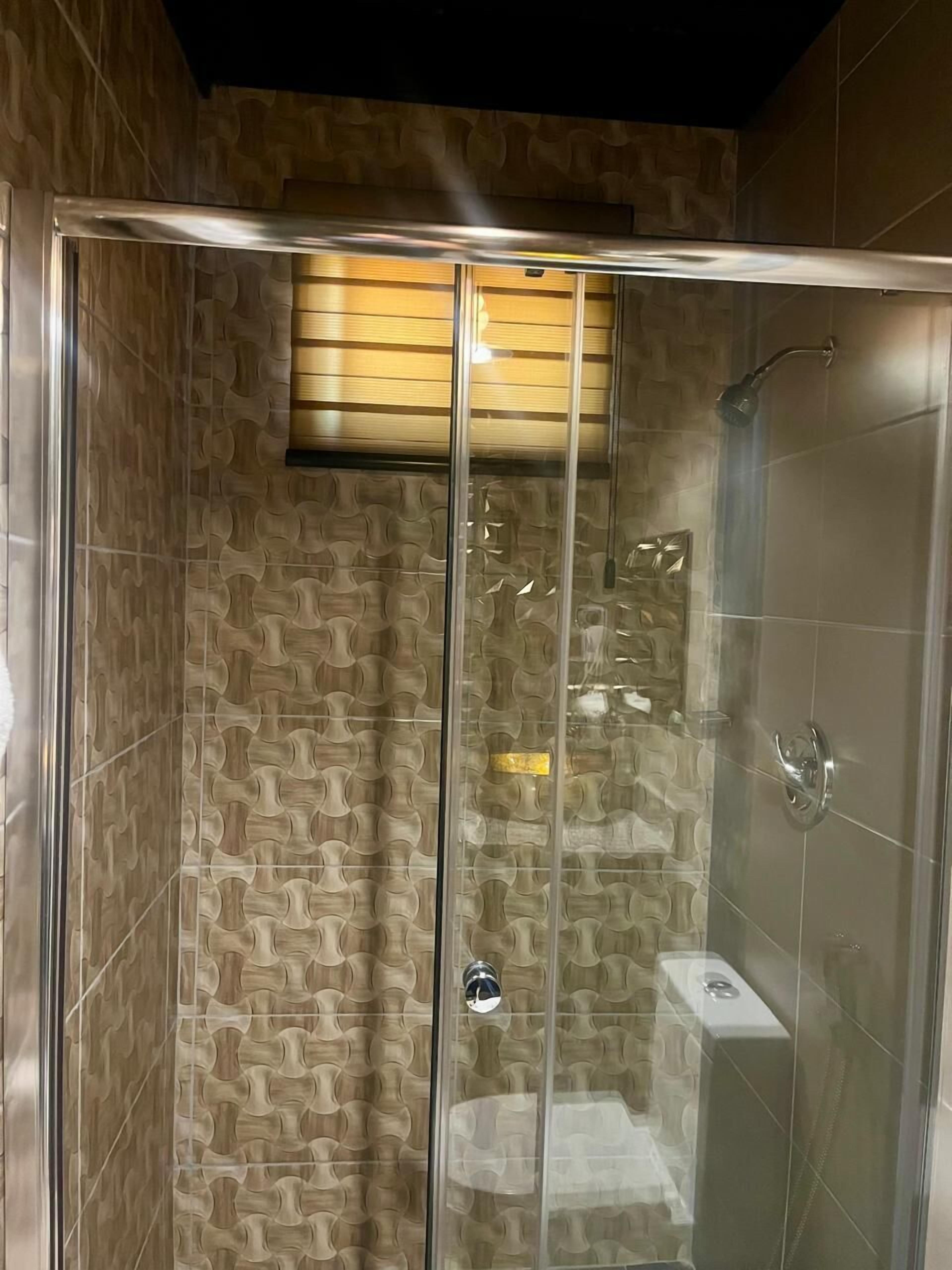 A glass-enclosed shower with a wooden panel above the door and a showerhead on the right.