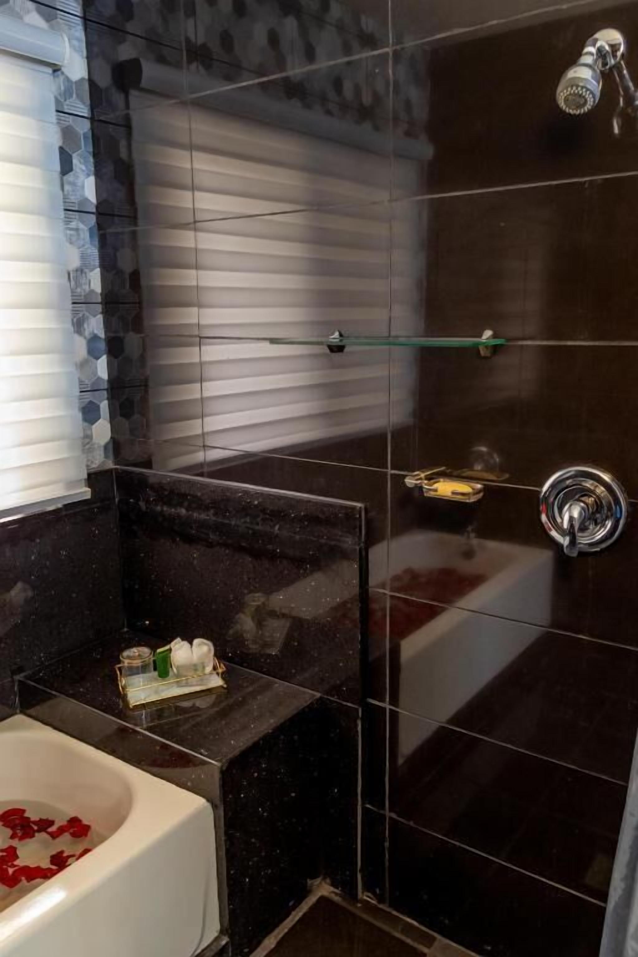 A modern bathroom with a glass shower enclosure, a white bathtub with rose petals, and a small shelf with toiletries.
