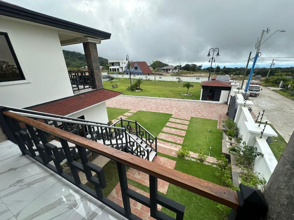 A residential area with a staircase leading to a balcony, a paved courtyard, and a view of surrounding houses.