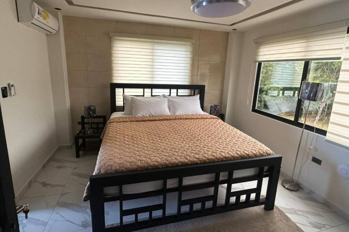 Une chambre à coucher avec un lit, un ventilateur de plafond, une fenêtre avec des stores et une vue sur l’extérieur.