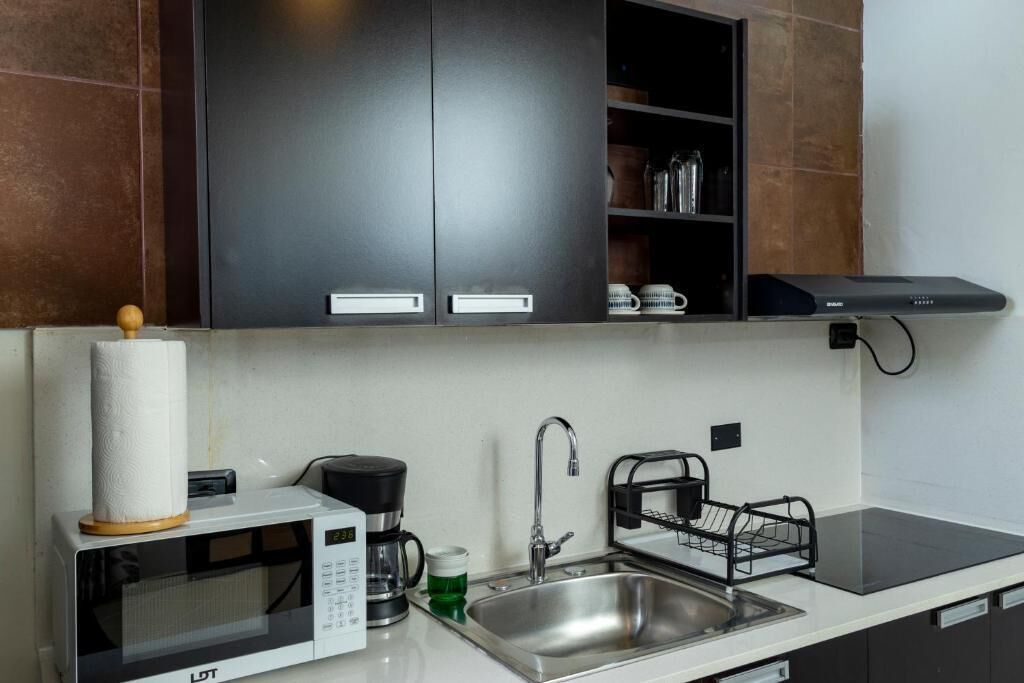 Una cocina moderna con microondas, cafetera, pileta y alacenas negras.