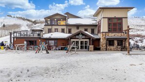 A lodge with a ski lift in the background, a dining area, and a stone building with a sign. - Luxury 1-bedroom ski in/ski out condo in lovely Granby Ranch (Granby)