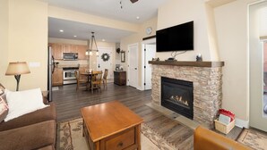 A living room with a fireplace, a television mounted above it, and a dining area in the background. - Luxury 1-bedroom ski in/ski out condo in lovely Granby Ranch (Granby)