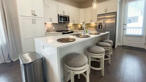 Een moderne keuken met witte kasten, een roestvrijstalen koelkast, een inbouwmagnetron en een groot eiland met barkrukken.