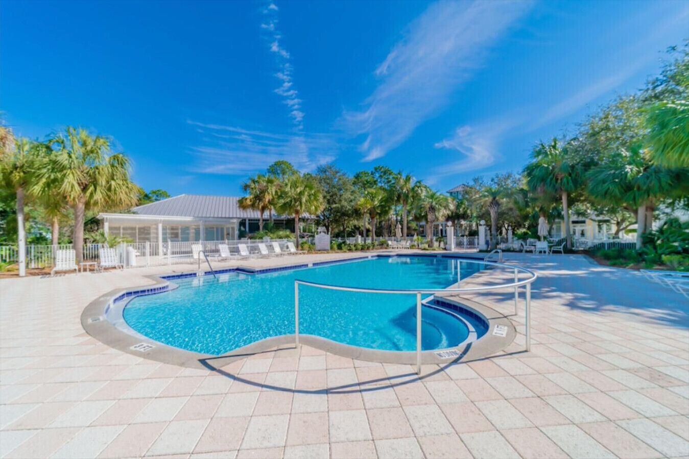 Una piscina de diseño curvo, rodeada de palmeras y sillones de descanso.