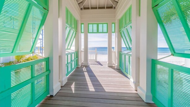Un pasillo de madera cubierto con contraventanas verdes que da a la playa.