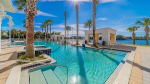 Una gran piscina al aire libre con agua cristalina y azul, rodeada de palmeras y un edificio blanco con un área de estar cubierta.