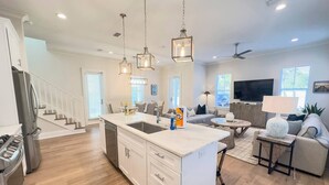A modern kitchen with a central island, a dining area with a round table, and a living room with a sofa and a TV.