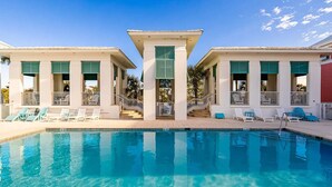 Una piscina con sillones de descanso y una escalera que conduce a un edificio con fachada blanca y contraventanas verdes.