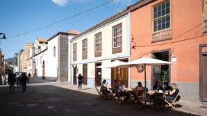 Una calle con mesas al aire libre en un café, edificios de arquitectura tradicional y cielo despejado.