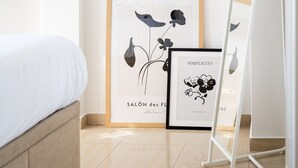 Un dormitorio con una cama, un grabado botánico enmarcado y un espejo de pie.