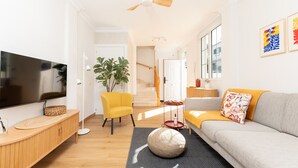 Una sala moderna con televisor de pantalla plana, un sofá, un sillón amarillo y una escalera que sube a otra habitación.