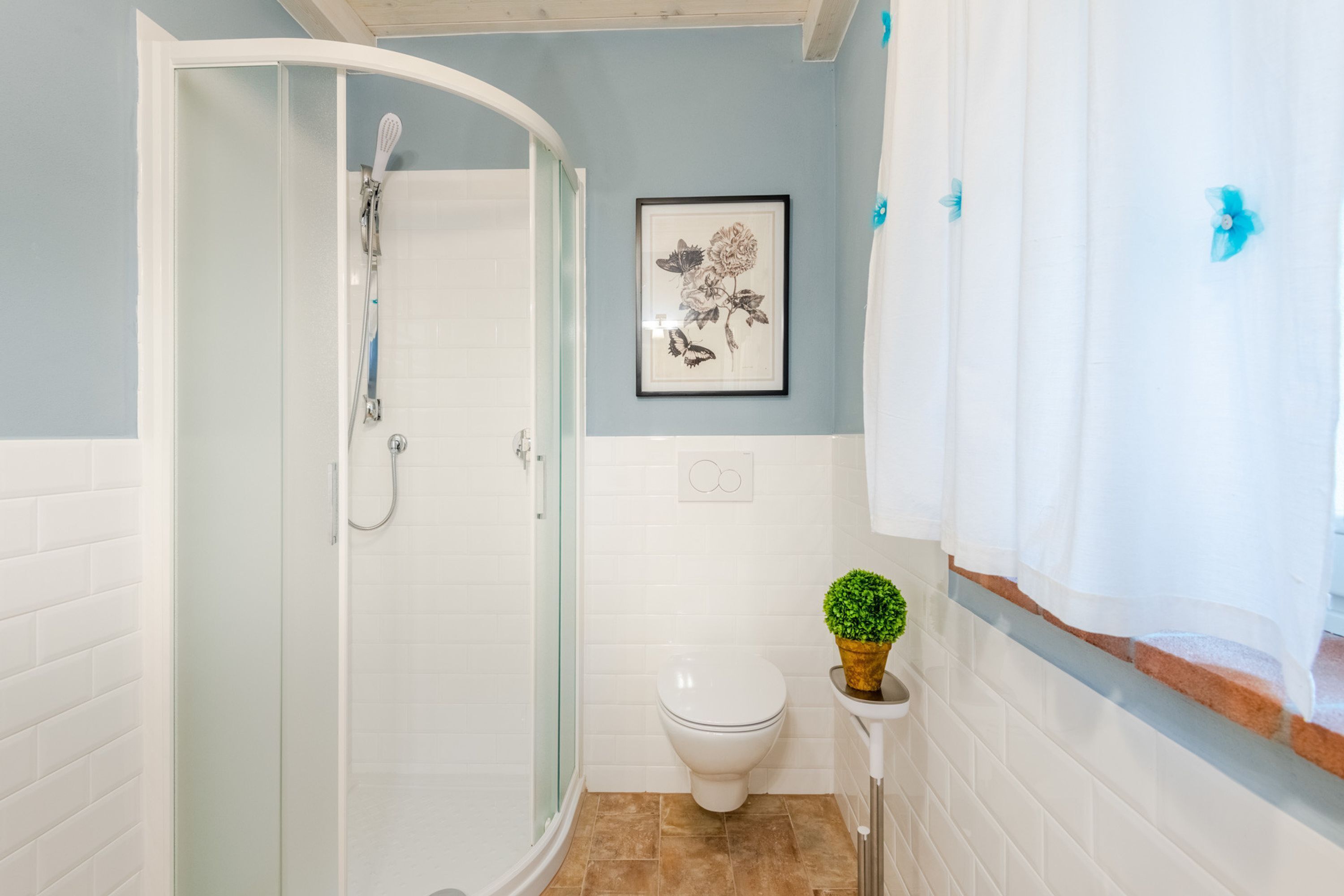 A bathroom with a glass-enclosed shower, a toilet, and a framed floral artwork on the wall.