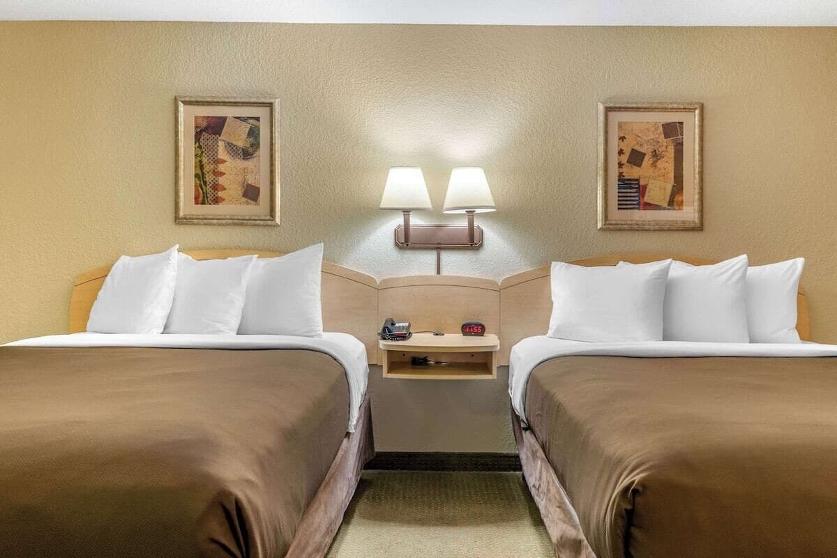 Habitación de hotel con dos camas, una mesita de noche, dos lámparas de pared y obras de arte enmarcadas.