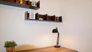 A wooden desk with a lamp, a potted plant, and shelves above holding decorative items. - 1br, Balcony, Cityview, Office, Ws98 (London)